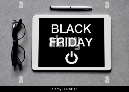 high-angle shot of a pair of eyeglasses, a pen and a tablet computer text black friday written in its screen placed on a gray su Stock Photo