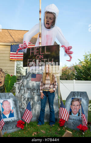 Bellmore, United States. 02nd Nov, 2016. Bellmore, New York, USA. November 2, 2016. EILEEN FUSCALDO, a Donald Trump Supporter, stands in a graveyard display in her Halloween front yard display with a large Hillary Clinton Ghost with 'Hell on Earth' sign looming over Fuscaldo's head, and tombstones with photos of Americans killed in Benghazi. Her Halloween yard decorations had many signs and disaplys in support of the Republican presidential candidate D. J. Trump, and against Democratic H. R. Clinton. Credit:  Ann E Parry/Alamy Live News Stock Photo