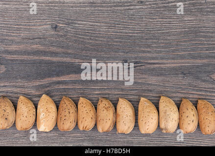 Raw almonds in their shells arranged in a row on a wooden background with copy space for your text Stock Photo