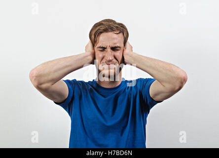 Sad Young Adult Male in Blue T-Shirt Covers His Ears Stock Photo