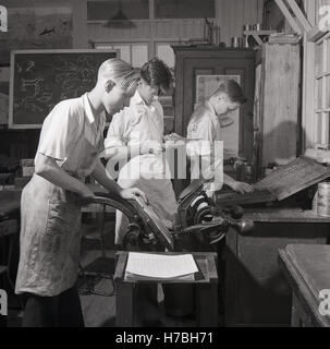 1950s, historical, London, England. Young male apprentices in a printing workshop, one using a manual press, for letterpress printing, another assembling metal type into words and lines with a composing stick. Stock Photo