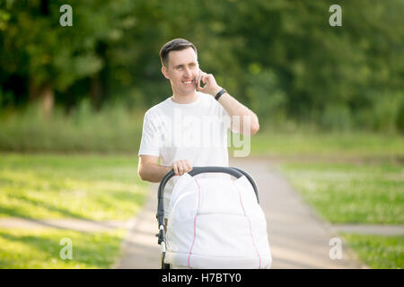 Father walking with carriage and talking on phone Stock Photo