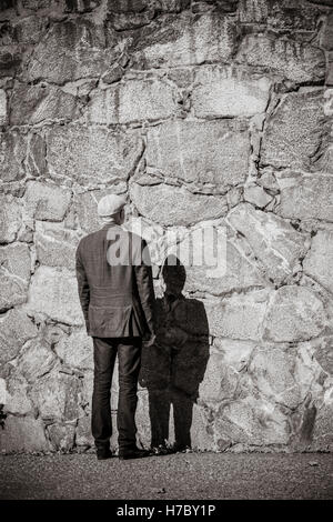 Old man standing in front of stone wall. Sunshine and heavy shadow. Building exterior with copy space. Stock Photo