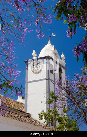 Portugal, the Algarve, Moncarapacho village church clock tower and jacaranda tree in flower Stock Photo