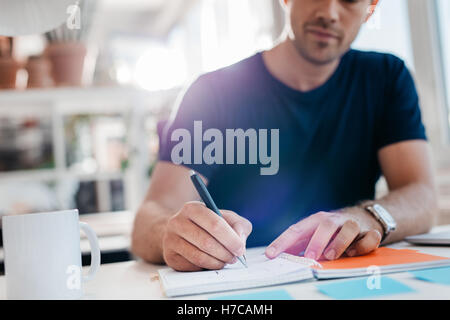 Young businessman writing down important notes in diary at his desk. Young businessman writing in his notepad. Stock Photo