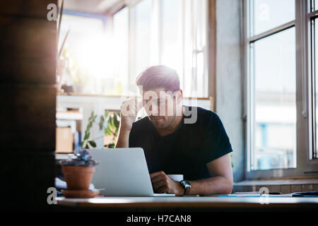 Young man working on the laptop in the office. Business man thinking about a problem at his computer. Stock Photo