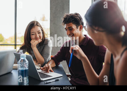 Indoor shot of three young students studying together using laptop. university students smiling and using laptop in college libr Stock Photo