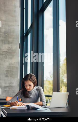 Female student taking notes from books for her study. Young woman sitting at table with books at university library. Stock Photo