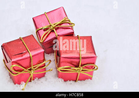 three small red metallic bright parcels on snow background, close up, space for text, horizontal Stock Photo