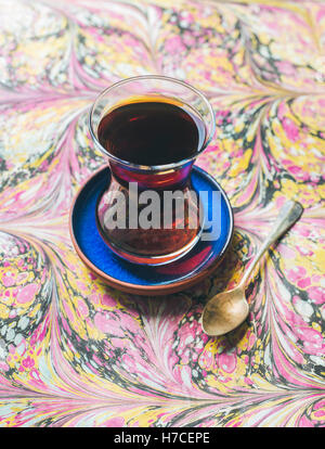 Turkish tea in traditional oriental tulip glass over ebru painted colorful paper background, selective focus, vertical compositi Stock Photo