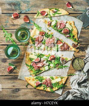 Fig, prosciutto, arugula and sage flatbread pizza cut into pieces with glasses of rose wine over rustic wooden background, top v Stock Photo