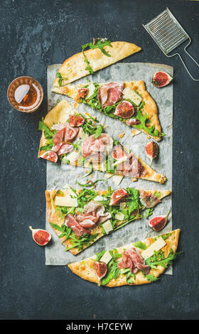 Fig, prosciutto, arugula and sage flatbread pizza cut into pieces with glass of rose wine over black grunge stone background, to Stock Photo