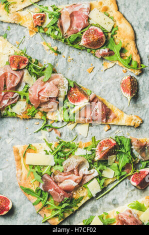 Pieces of fig, prosciutto, arugula and sage flatbread pizza on baking paper, top view, vertical composition Stock Photo