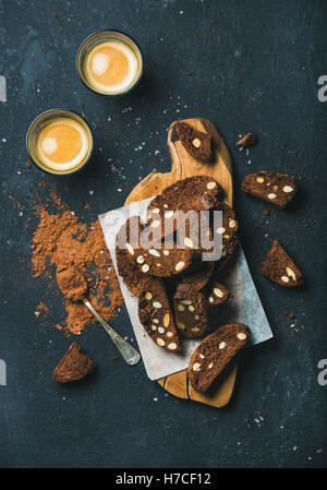 Dark chocolate and sea salt Biscotti with almonds on wooden serving board and two glasses of coffee espresso over dark stone bac Stock Photo