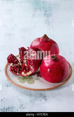 Ripe slice and whole pomegranates on ornate ceramic plate over white wooden background. Stock Photo