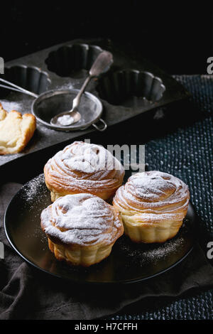 Modern pastries cruffins, whole and slice, like croissant and muffin with sugar powder, served on black plate with sieve, silico Stock Photo