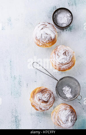 Modern pastries cruffins, like croissant and muffin with sugar powder, served with vintage sieve over white wooden background. T Stock Photo