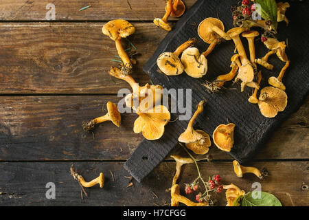 Forest Chanterelle mushrooms with wild raspberries on black wood cutting board over old  wooden background. Top view, copy space Stock Photo
