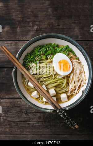 Ceramic bowl of asian style soup with green tea soba noodles, egg, mushrooms, spring onion and tofu cheese, served with chopstic Stock Photo