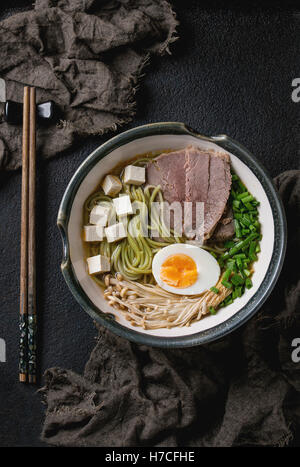 Bowl of asian style soup with green tea soba noodles, beef, egg, mushrooms, spring onion and tofu cheese, served with chopsticks Stock Photo