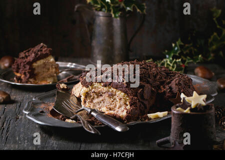 Sliced homemade Christmas chocolate yule log with chestnuts cream on vintage plate with forks,  chocolate stars and holly branch Stock Photo