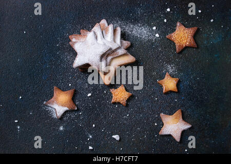 Homemade shortbread star shape sugar cookies different size with sugar powder on black textural surface. Christmas treats backgr Stock Photo