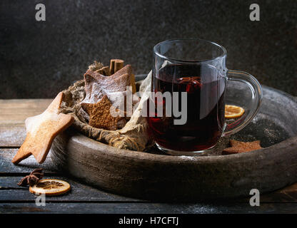 Glass mug of hot red mulled wine spices, sugar shortbread cookies star shape, anise and cinnamon powder in clay tray with sackcl Stock Photo
