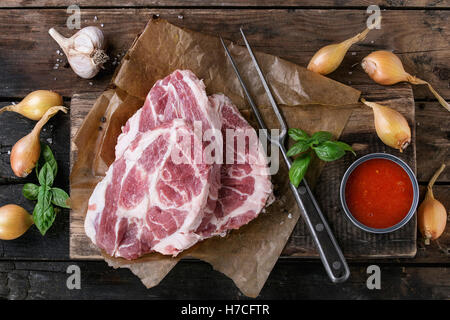 Raw steak meat pork neck on chopping board with shallot onion, tomato sauce marinade, basil and seasoning, served with meat fork Stock Photo