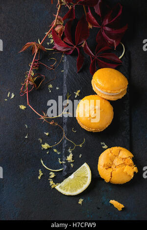 Whole and broken orange lemon homemade macaroons with white chocolate, lemon slice and zest, citrus sugar on slate board with au Stock Photo