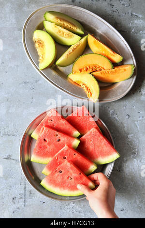 Fresh sliced melons on plates.Female hands holding a slice of watermelon. Stock Photo