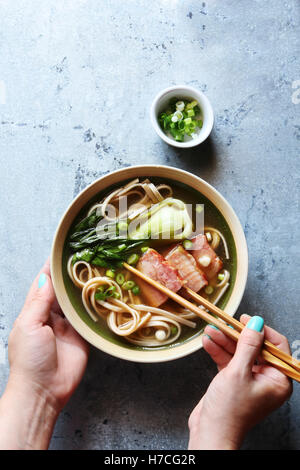 Female hands holding a bowl of pork belly udon noodle soup.Top view Stock Photo