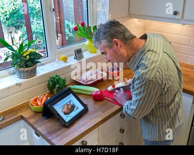 Man preparing roast chicken meal in contemporary home kitchen using tablet computer to provide an on-line recipe Stock Photo