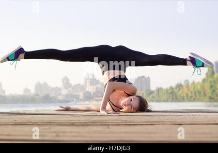 Young pretty slim fitness sporty woman doing streching yoga exercise during training workout outdoor at river coast in the morni Stock Photo