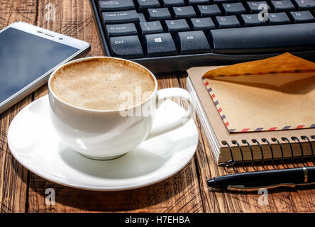 notepad, pen,phone, envelope, keyboard and coffee cup on an old wooden table Stock Photo
