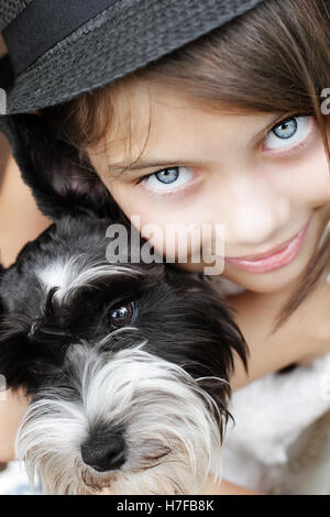 Young girl looking directly into the camera, wearing a fashionable black hat and snuggling her puppy. Stock Photo