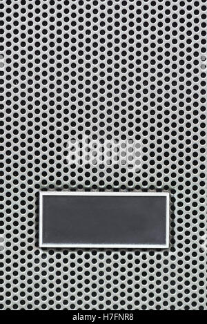 Metal plate label on metal steel grid with repetitive rows of punched circular holes, background and texture, Metal Grid for ind Stock Photo