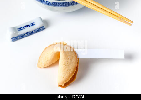 Fortune cookie with blank slip and Chinese bowl and chopsticks in background. Isolated on white. Stock Photo