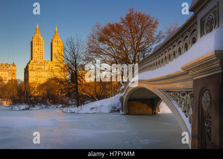 Central Park winter sunrise on the frozen Lake with the Bow Bridge and Upper West Side buildings. Manhattan, New York City Stock Photo