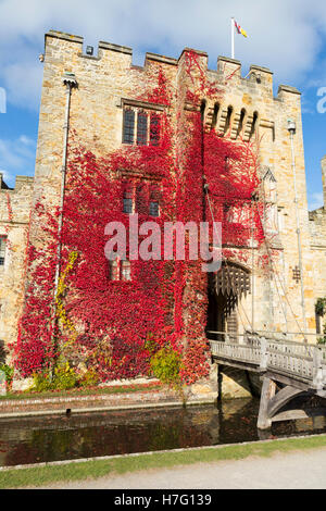 Hever Castle clad with red autumnal virginia creeper: Blue sky / sunny skies / sun & drawbridge / draw bridge over moat. Kent UK Stock Photo