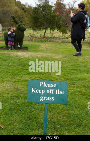 Please Keep off the grass / lawn sign, & people / tourists / tourist visitors / visitor ignoring the signs / breaking the rule.