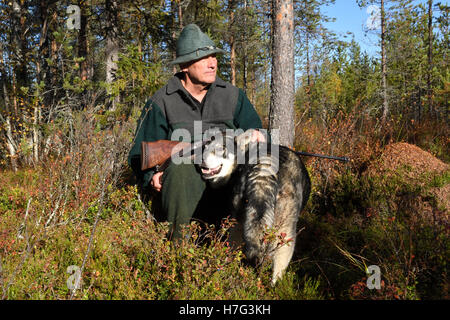 Moose hunter sitting on a stump holding his rifle and with his dog next to him,picture from the North of Sweden. Stock Photo