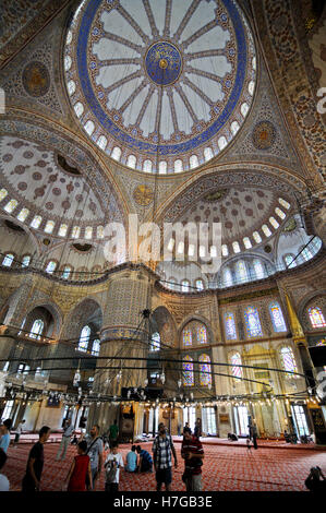 Blue Mosque, Istanbul. Wide angle view of the dome and copula from the inside with decoration, lamp and tourists Stock Photo
