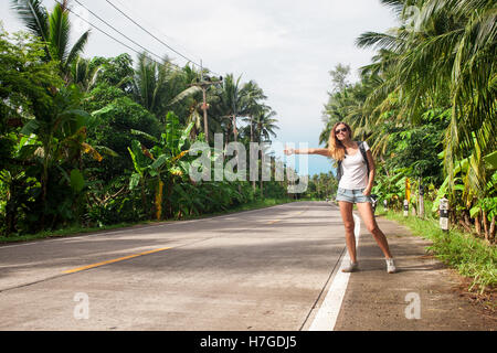 young woman hitchhiking along a road Stock Photo