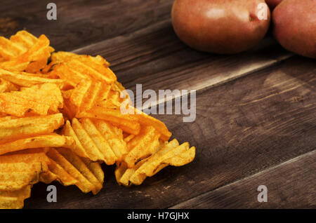 Heap of  potato chips with potato on rustic wooden background Stock Photo