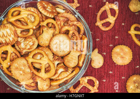 Mix of salty snacks (crackers and pretzels) in glass bowl on red background Stock Photo