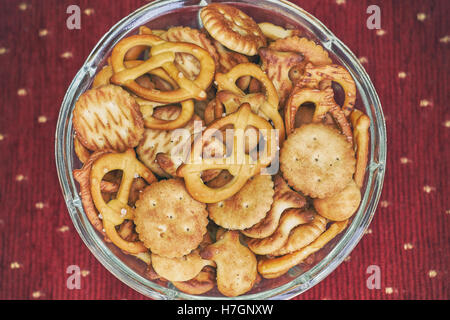 Mix of salty snacks (crackers and pretzels) in glass bowl on red background Stock Photo