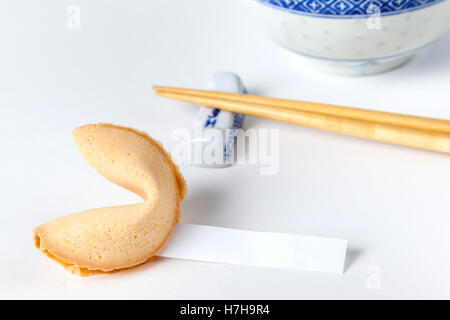 Fortune cookie with blank slip and Chinese bowl and chopsticks in background. Isolated on white. Stock Photo