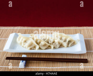 Gyoza or potstickers on a plate over a bamboo mat. Selective focus and deliberate shallow depth of field on background. Stock Photo