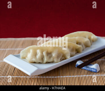 Gyoza or potstickers on a plate over a bamboo mat. Selective focus and deliberate shallow depth of field on background. Stock Photo
