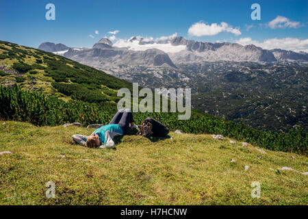 Young female hiker lying on grassy slope. Mountains and glacier on background Stock Photo